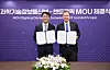 Two men in suits hold open signed documents in front of a purple event backdrop and flower arrangement.