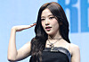 An Yu-jin poses on stage in a black outfit at an album showcase with a blue backdrop.