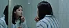 Woman applying lipstick while looking into a bathroom mirror.