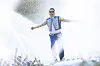 A singer stands onstage with arms outstretched as water sprays around him at a concert.