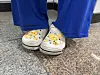 White clogs with cartoon duck designs worn with blue pants on a speckled tile floor.