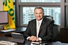 Suited executive seated at a desk in an office with a laptop, window view, and yellow flag.