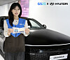 Woman holding a GS25 card beside a black Hyundai Grandeur with GS25 and Hyundai branding overhead.