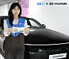 Woman holding a GS25 card beside a black Hyundai Grandeur with GS25 and Hyundai branding overhead.