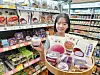 CU employee holds ube dessert products beside a display of purple-themed breads and sweets in a convenience store.