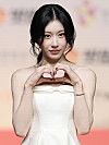 ITZY's Chaeryeong in a white strapless dress poses with a heart gesture on a red carpet.