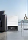 White LG robot vacuum station beside a sofa and side table in a minimalist living room.