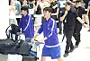 A football player in a blue tracksuit walks with luggage through Incheon airport, followed by staff and photographers.