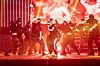 Performers dancing on a stage with bright red lights and smoke.