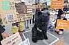 Protesters in Seoul display signs beside a person in a bear costume during a rally.