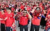 Crowd of fans in red cheering with hands on their heads during a street viewing in Seoul.