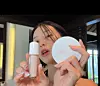 Woman holding a cosmetic tube and a round eylin compact indoors.