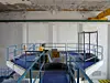 Empty reactor hall with blue-railed platforms, metal equipment, and a worn ceiling inside a large industrial room.