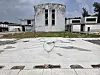 An old concrete reactor building and low auxiliary structures stand in an open paved lot under a cloudy sky.
