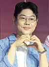 A man in glasses makes a heart gesture at a Netflix press conference backdrop.