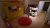 Person standing beside a lit shelf in a room with a red rug and colorful wall panels.