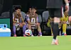 Football substitutes seated on the bench behind a player standing on the field.