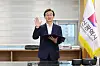 A man in a suit raises one hand while holding a folder during an oath ceremony indoors beside a Busan flag.