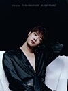 Portrait of a person in a black satin outfit posing against a dark background.
