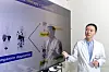 A doctor in a white coat gestures beside a large medical presentation screen in a hospital room.