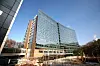 A modern glass hospital building with a curved facade stands under a clear blue sky.