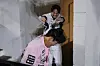 A smiling baseball player in white reaches out in a hallway as a person in a pink jacket leans forward.