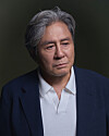 Studio portrait of an older man with gray hair wearing a dark blazer and white shirt.