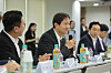 A man in a suit speaks at a conference table with water bottles and microphones during a meeting.