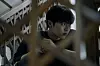 Choi Hyun-wook as Lee Kang crouches in a dark, framed shot with blurred lattice patterns in the foreground.
