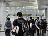Travelers walking through a bright airport terminal under digital flight information signs.