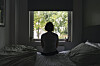 A woman gazes at a window inside a bedroom.