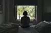 A woman gazes at a window inside a bedroom.