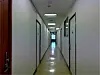 Long empty corridor with white walls, doors on both sides, and overhead fluorescent lights.