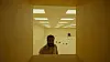 A man seated in a simple indoor space viewed through a rectangular opening.