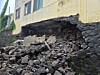 Collapsed foundation with rubble piled beneath a damaged building wall.