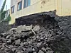 Collapsed foundation with rubble piled beneath a damaged building wall.
