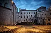 Empty rows of chairs in a stone courtyard amphitheater inside a historic fortress at dusk.