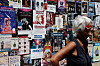 Woman walking past a wall covered in colorful Avignon Festival play posters.