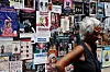 Woman walking past a wall covered in colorful Avignon Festival play posters.