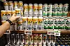 Shelves of Japanese beer cans in a Seoul supermarket, with a shopper reaching toward the display.