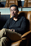 Man with glasses seated in a brown leather chair inside a modern room.