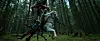 A white horse with a rider stands in a forest beside another person.