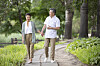 Two adults walking on a curving path in a green park with trees and plants.