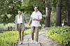 Two adults walking on a curving path in a green park with trees and plants.