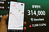 Hand holding a phone with a stock chart beside a display showing Samsung Electronics at 314,000 won.