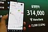 Hand holding a phone with a stock chart beside a display showing Samsung Electronics at 314,000 won.