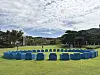 Blue blocks arranged in a circle on green grass with trees, hills and buildings under a cloudy sky.