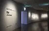 Dark exhibition corridor with wall text and projected light patterns.