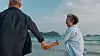 Senior couple holding hands and walking on a beach near the water.