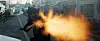 Person firing a handgun on a city street with a bright muzzle flash.